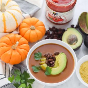 orange pumpkin, white and orange striped pumpkin, jar of salsa, avocados, black beans, bowl of pumpkin soup topped with beans, avocado and cilantro
