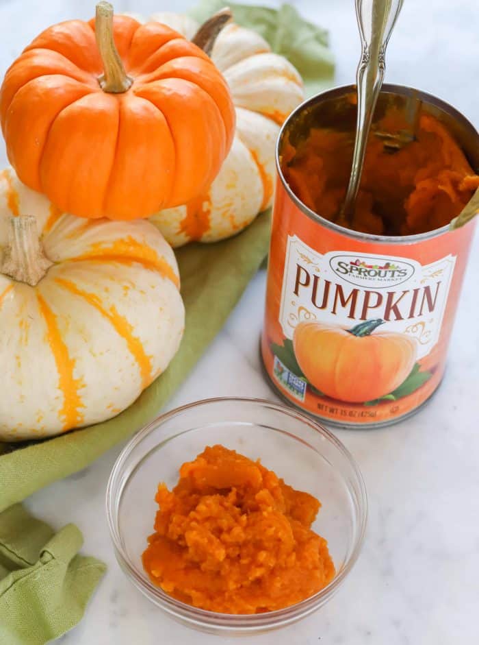 small white and orange pumpkins on green napkin, small clear bowl of pumpkin puree, can of pumpkin puree with silver spoon in it