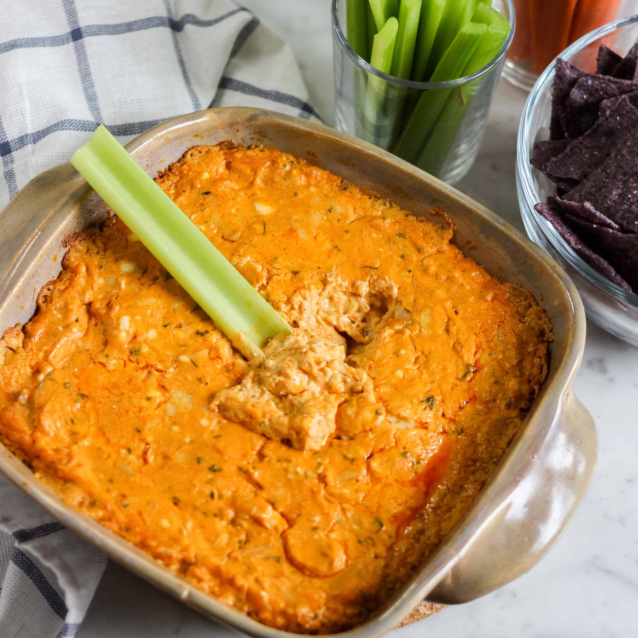 celery stick dipping into a square baking dish with buffalo chicken dip