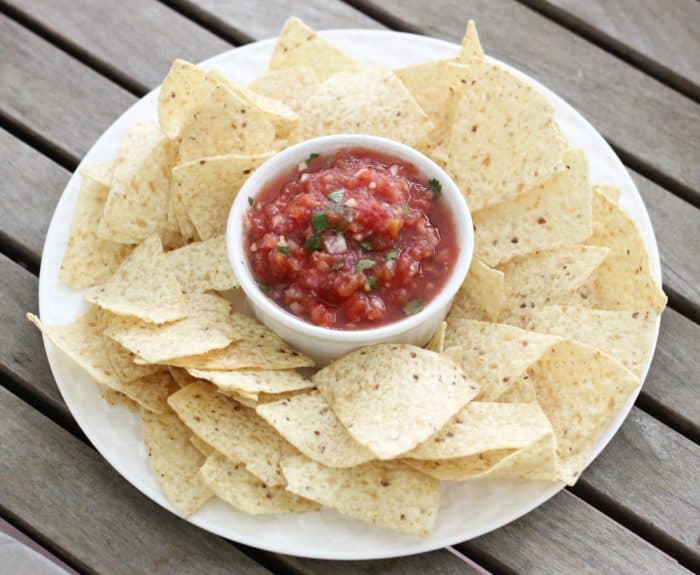 wooden table with white plate full of chips and a bowl of homemade salsa