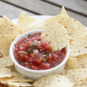plate of chips with bowl of salsa and a chip sitting in salsa