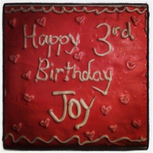 pink birthday cake that says "happy 3rd birthday Joy" in white icing.