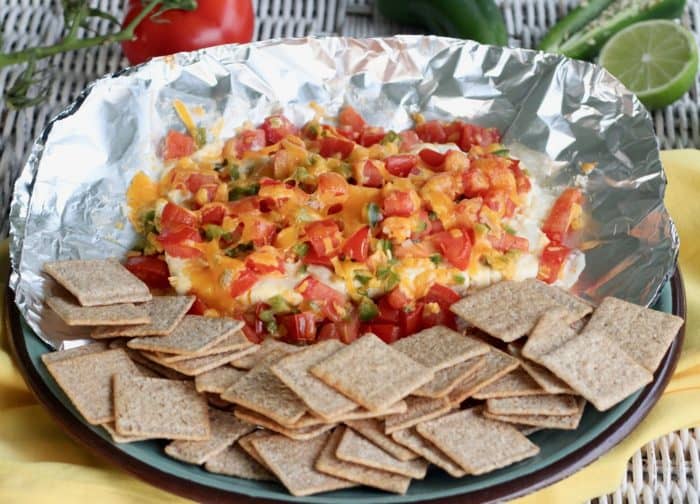 plate of cream cheese appetizer and whole grain crackers on a glass plate on a yellow napkin