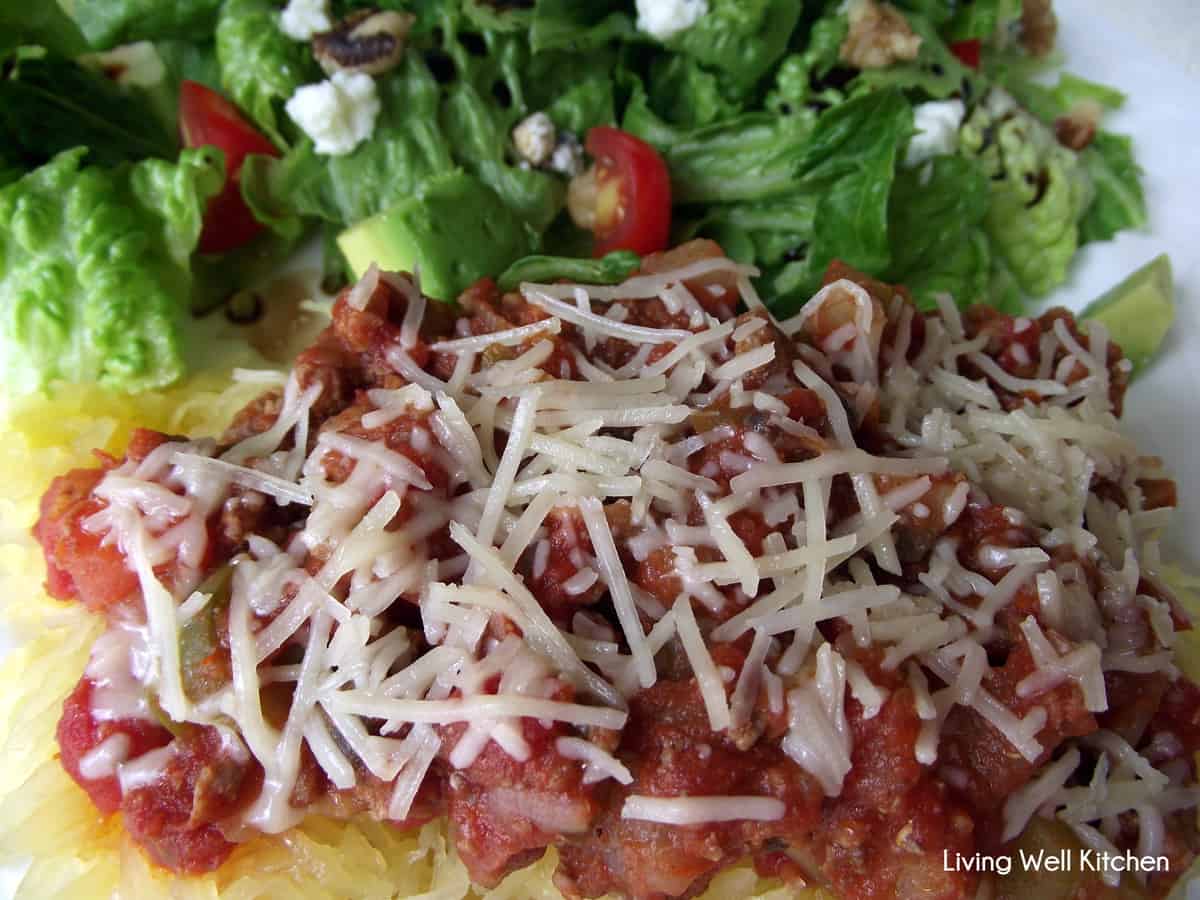 close up photo of spaghetti squash topped with turkey meat sauce and parmesan with a salad in the background