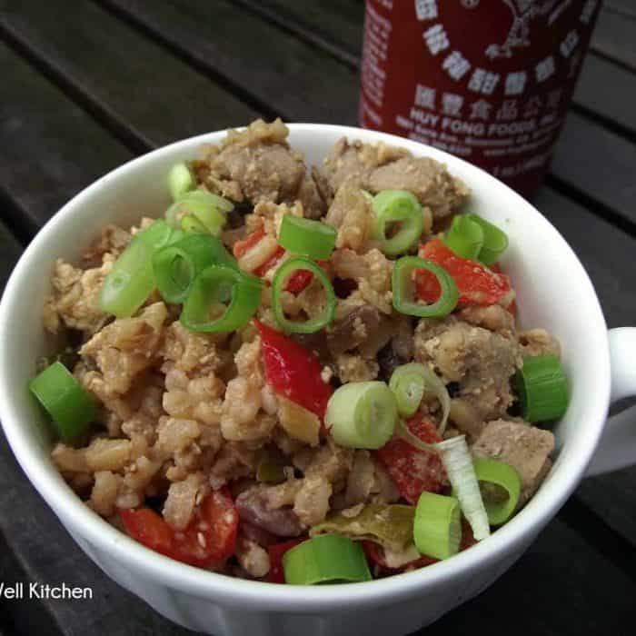 bowl of pork fried rice in a white cup with sriracha sauce