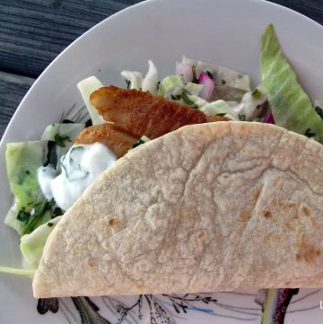 white patterned plate with fish tacos with cabbage slaw and yogurt sauce