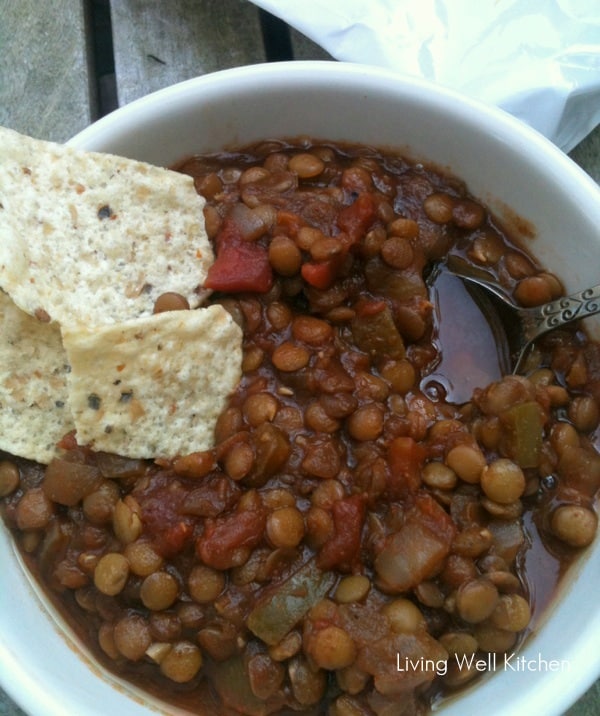 white bowl of lentil chili with tortilla chips and spoon sitting on wooden table