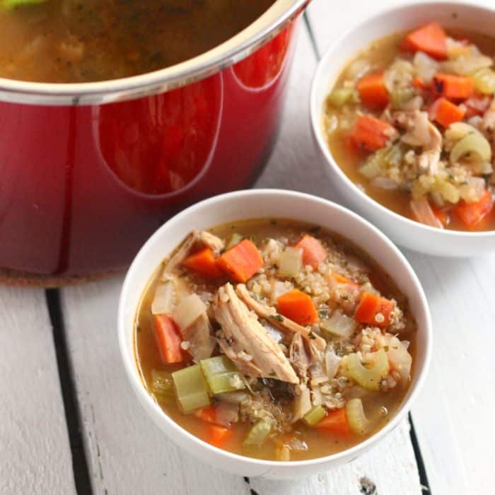 two white bowls of soup with turkey on white wooden table with red soup pot