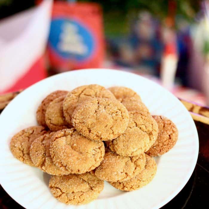 white plate of ginger cookies on brown table with Christmas tree and presents in background