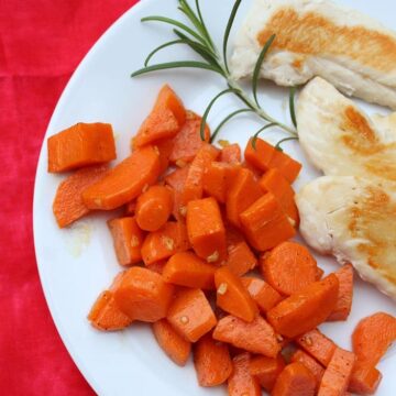 red napkin with cooked carrots, rosemary sprig, cooked chicken on a white plate