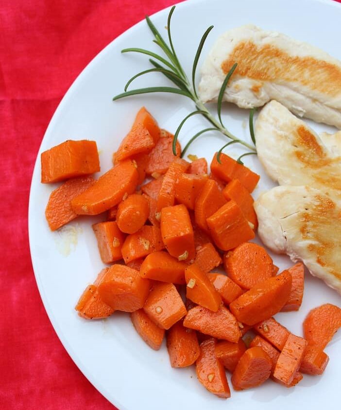 red napkin with cooked carrots, rosemary sprig, cooked chicken on a white plate 