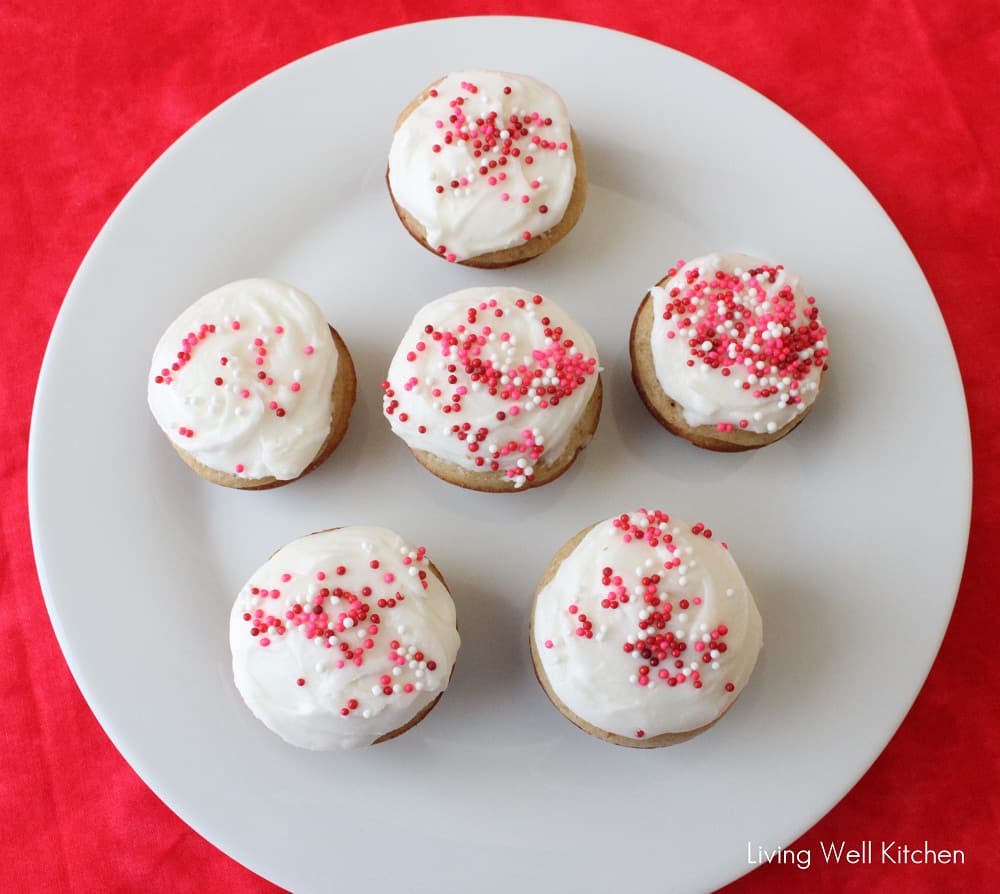 white plate on red tablecloth with mini small batch vanilla cupcakes topped with white frosting and pink, red, and white sprinkles.