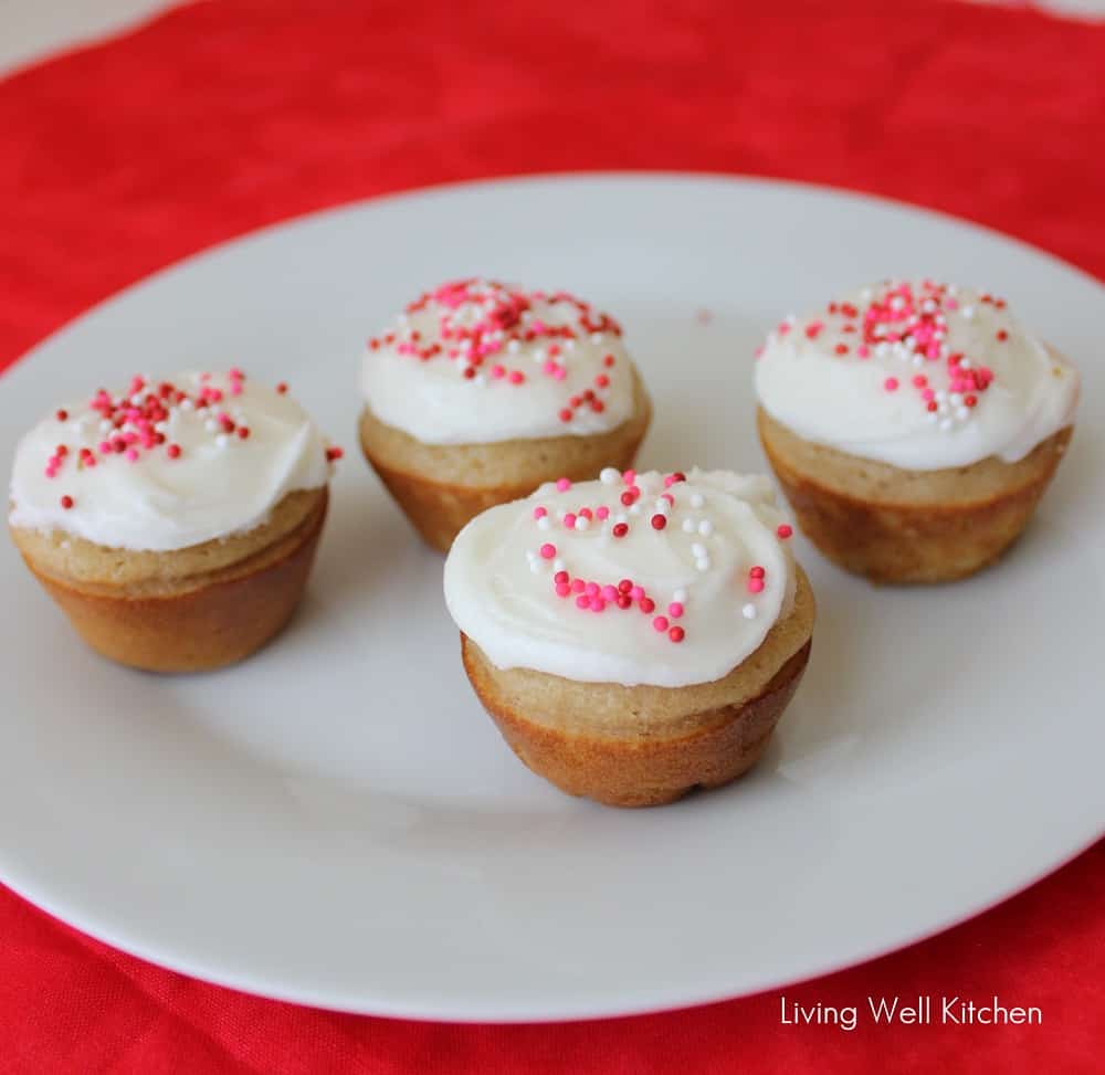 white plate with four mini cupcakes sprinkled with red, white, and pink sprinkles on white icing.