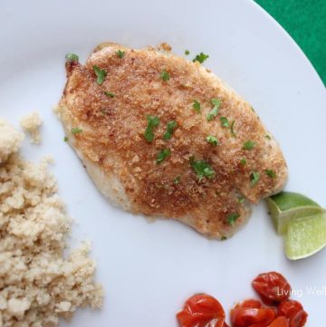 white plate on green napkin with Easy Baked Fish, lime slice, tomatoes and couscous