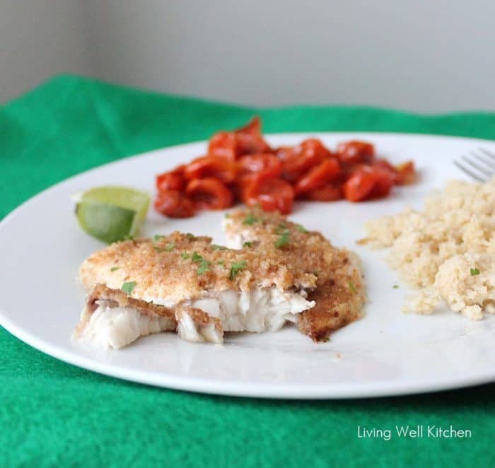 green placemat with white plate of flaked baked fish, couscous, tomatoes and lime slice