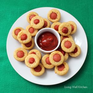 green table cloth with a white plate of mini corn dog muffins and a bowl of ketchup.