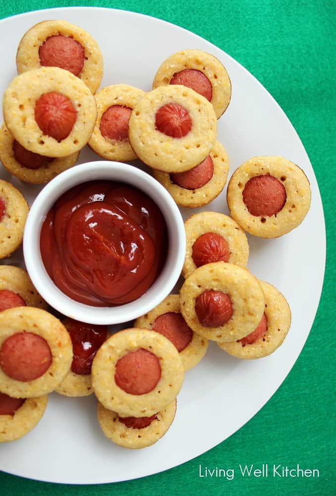 green tablecloth with white plate of mini corndog muffins and a bowl of ketchup.