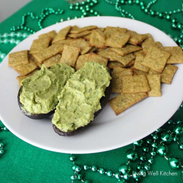 Spinach and Avocado Hummus in avocado skin with plate of homemade crackers on green tablecloth with green beads