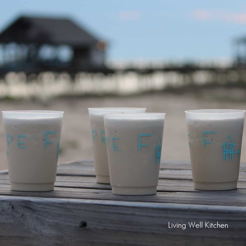 four plastic cups filled with bushwackers and a beach, Mobile Bar, and a wharf in the background