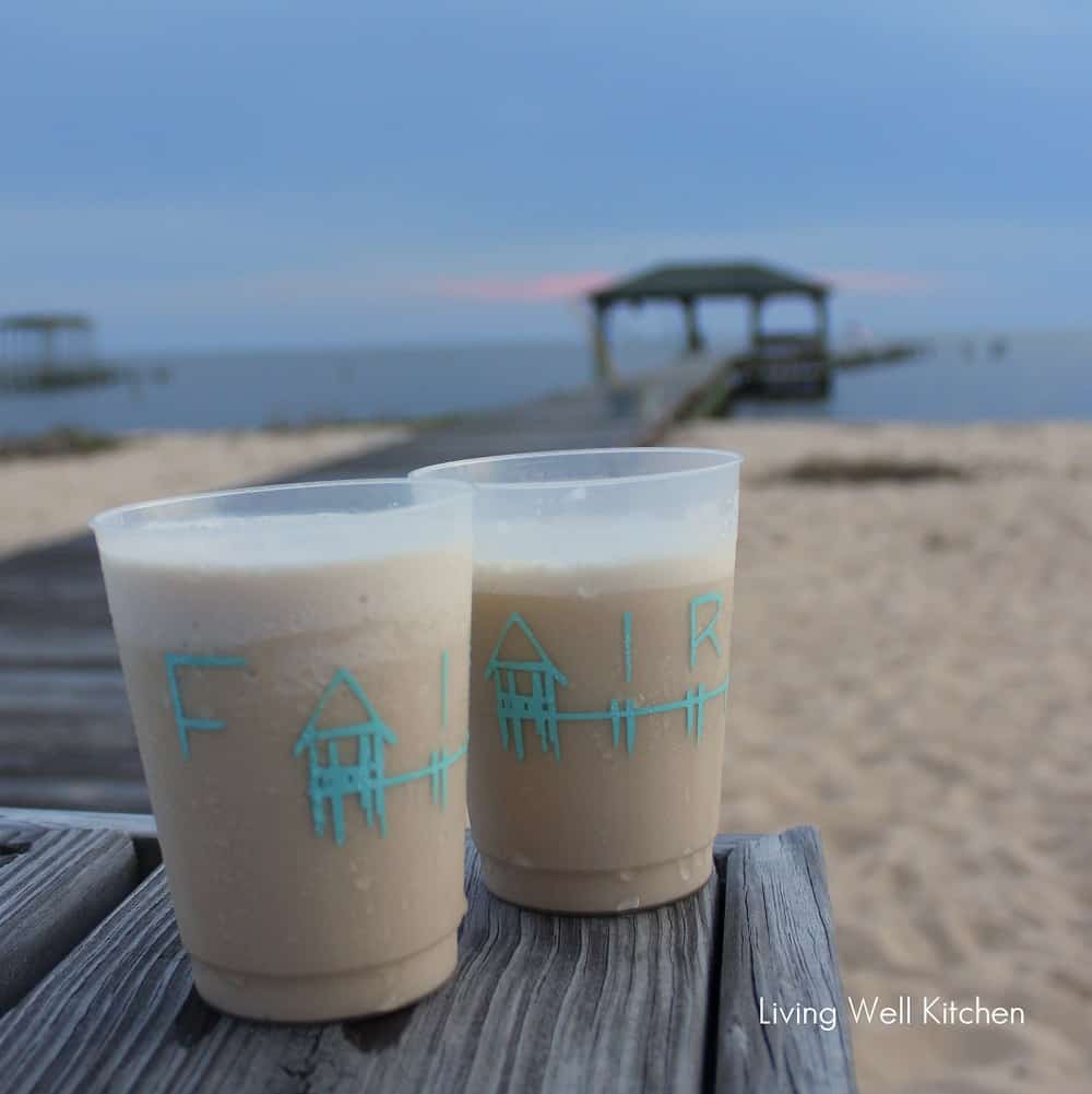 two plastic cups filled with a frozen drink and Mobile Bay and a wharf in the background