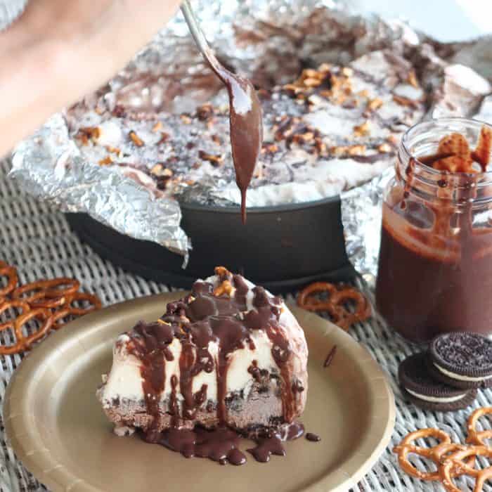 spoon drizzling chocolate sauce over ice cream pie with pretzels, oreos, and chocolate sauce