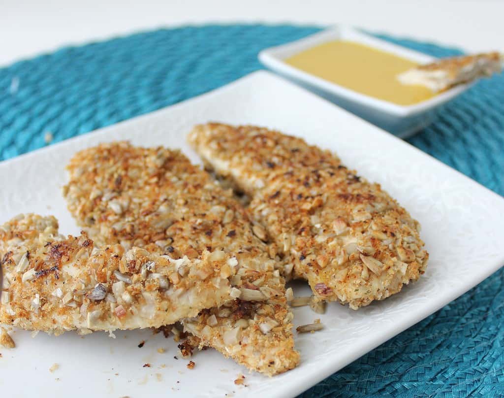 Sunflower Seed Crusted Chicken Fingers on a white plate and blue placemat