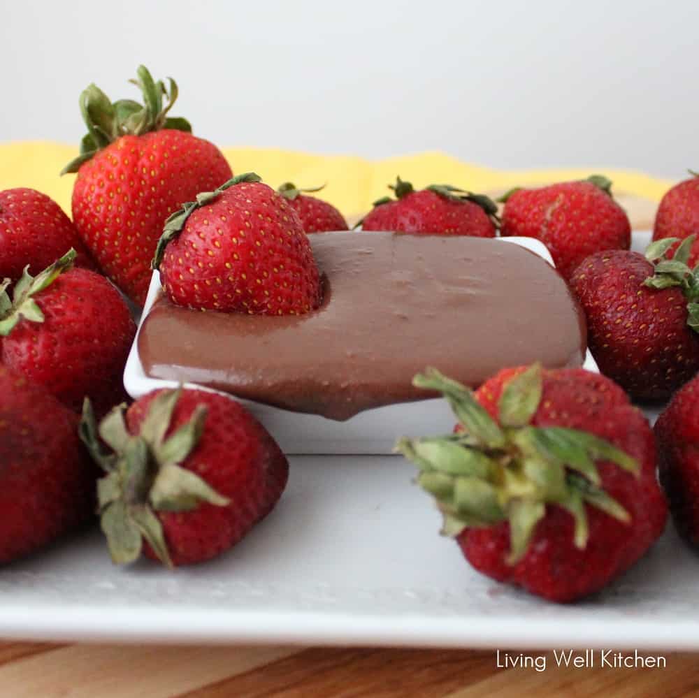 white plate with strawberries and a strawberry in a bowl of chocolate sauce spilling over the side