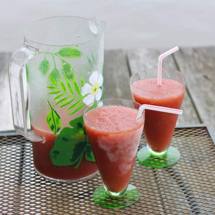 pitcher and two glasses of Red Roosters with straws on wooden pier with water in background