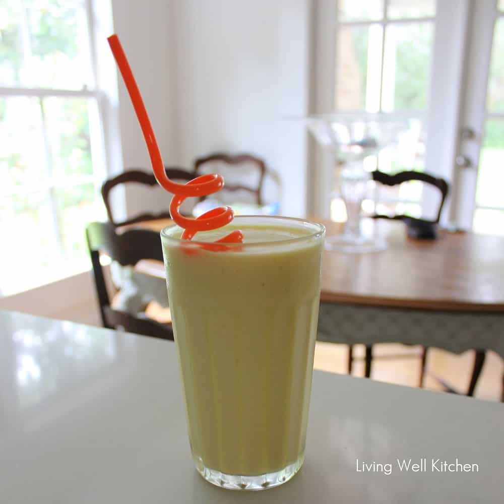 mango green tea smoothie in a glass with a swirly orange straw with a breakfast table in the background.