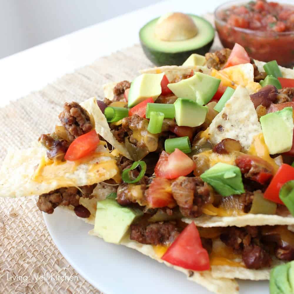 close up photo of nachos with beans, beef, cheese, avocados, and tomatoes