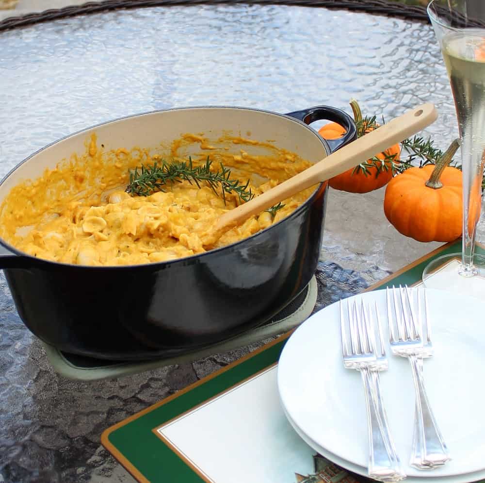 plates, forks, champagne, pumpkins, rosemary, and pot of mac and cheese with wooden spoon