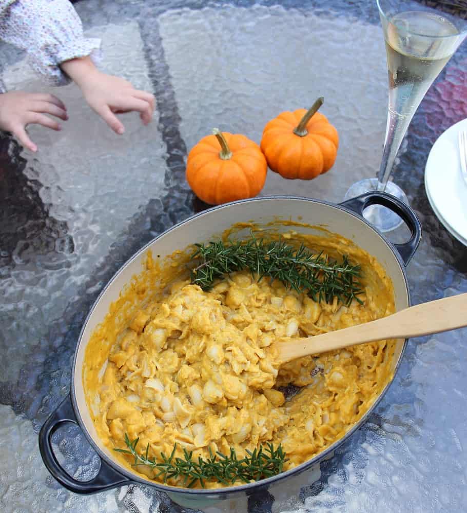 dutch oven with macaroni and cheese with rosemary on glass table with children's hands and small pumpkins