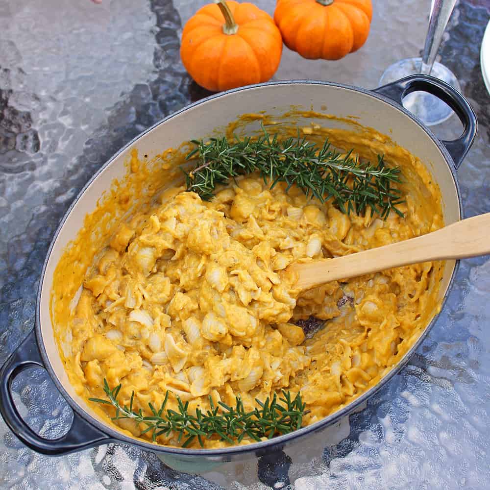 glass table with pot of mac and cheese with rosemary and two small pumpkins