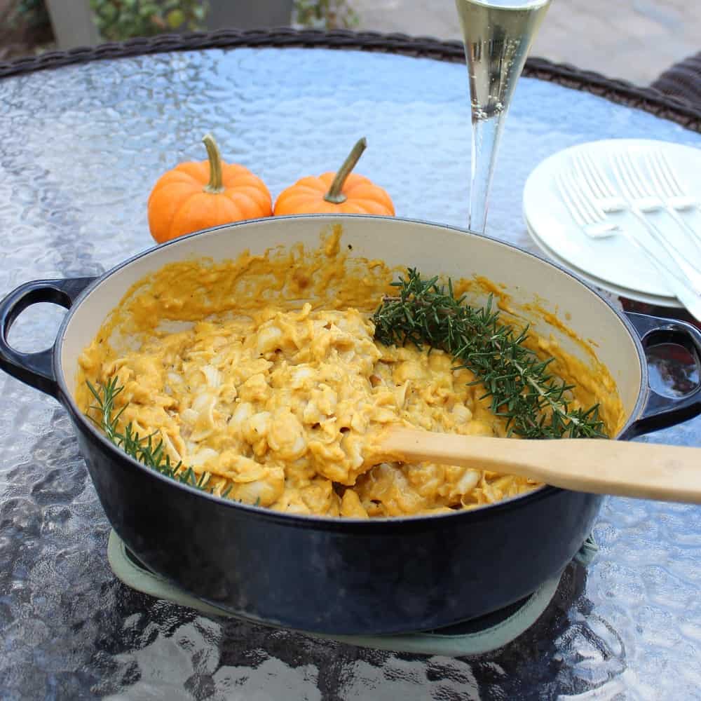 glass table with two small pumpkins, glass of champagne, forks and plates and a dutch oven full of mac and cheese topped with rosemary sprigs