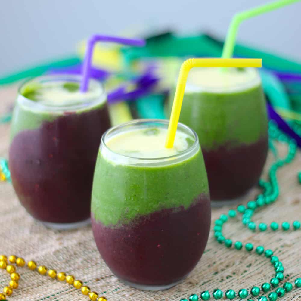 3 smoothies layered in yellow, purple, and green with straws and beads