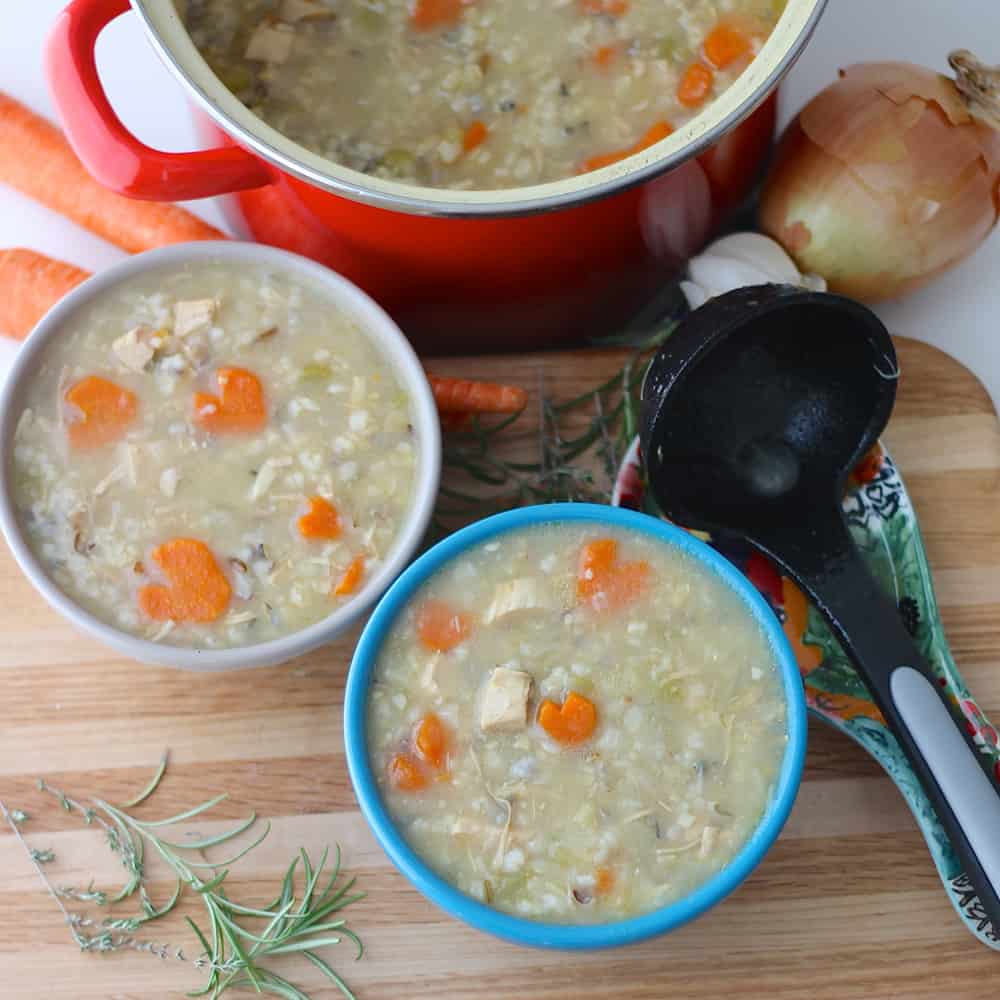 two bowl of Chicken and Rice Soup with a pot of soup, ladle, and herbs.