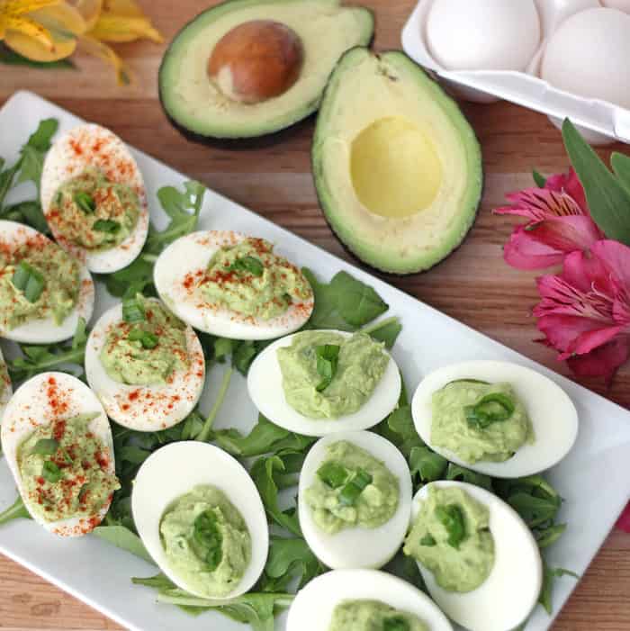 wooden cutting board with flowers, avocado, eggs, and plate of avocado deviled eggs