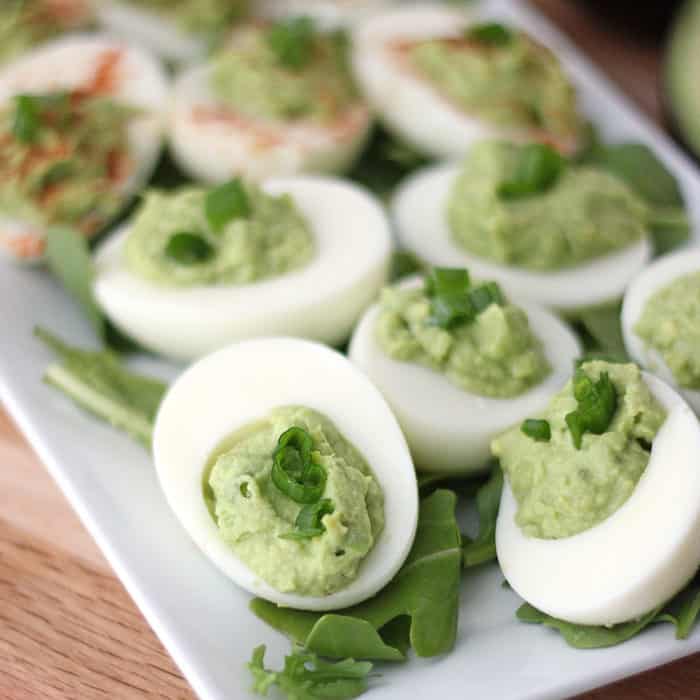 wooden table with white plate of arugula and avocado deviled eggs