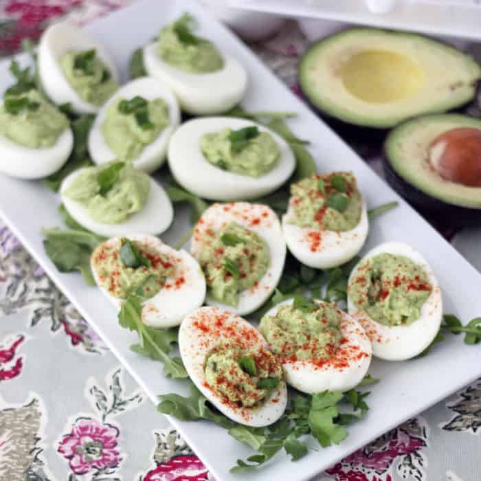 rectangular white plate with arugula and avocado deviled eggs surrounded by avocado and eggs