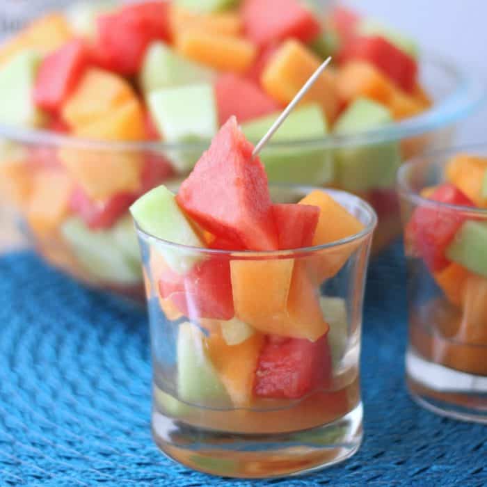glass with chopped watermelon, cantaloupe, and honeydew with toothpick, on blue placemat 