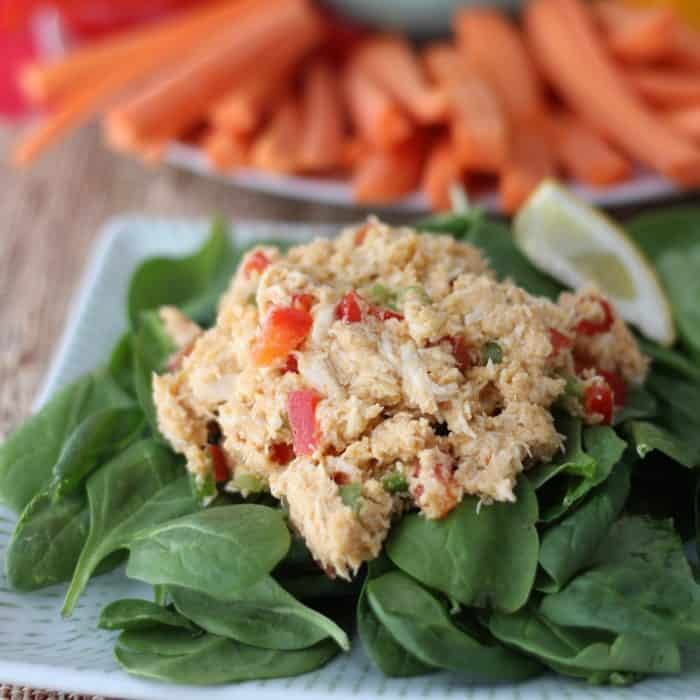 plate of spinach topped with hummus chicken salad and carrots in background