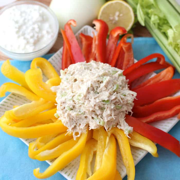 plate of red and yellow bell peppers and a scoop of chicken salad on blue table cloth with cottage cheese, onion, lemon and celery