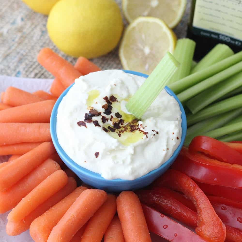 sliced bell peppers, celery and carrots, lemons, and blue bowl with lemon feta dip and celery