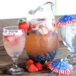pitcher of sangria and a glass of red white and blue sangria with a strawberry on glass with 4th of July drink umbrellas