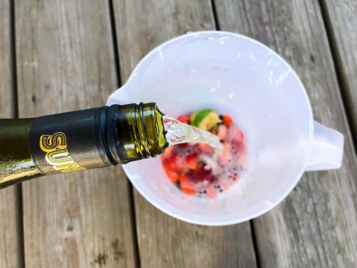 white wine pouring out of the bottle in a pitcher of fruit