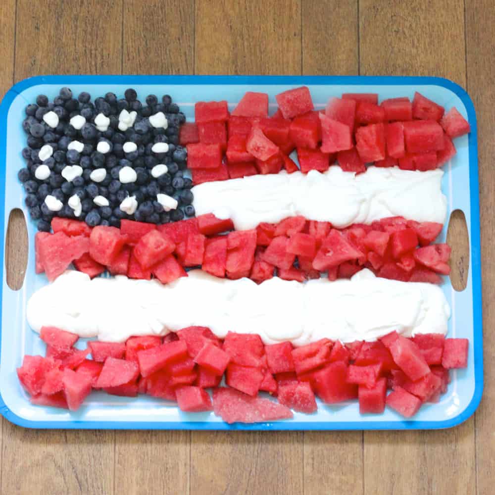 blueberries, watermelon and whipped cream in an American flag shape on a blue platter on wooden background