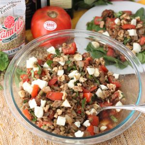 clear bowl with lentils, mozzarella, walnuts, tomatoes, and basil on a straw mat