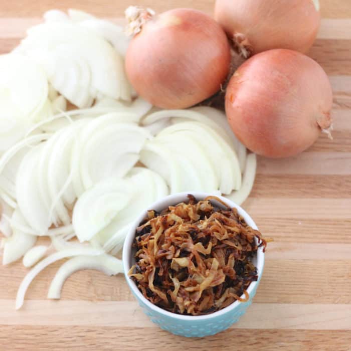 Caramelized Onions in a bowl on wooden cutting board with sliced onions