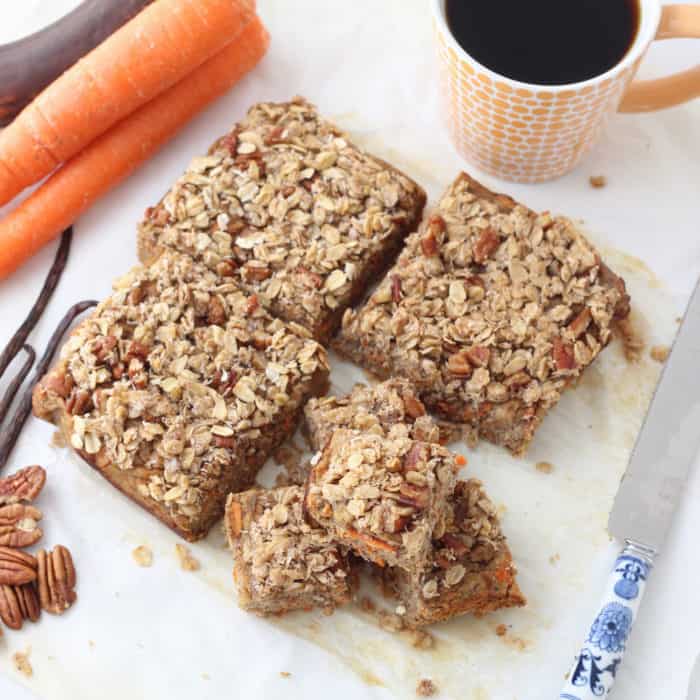 Coconut Carrot Coffee Cake with crumb topping cut into squares on parchment paper with knife, carrots, ripe banana, pecans, tea