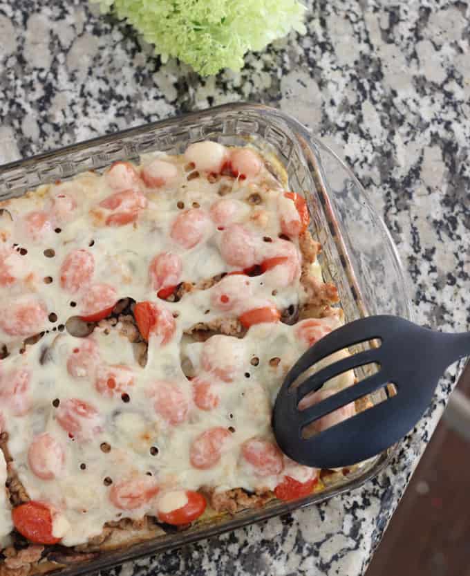 slotted spoon cutting Veggie and Swiss Breakfast Casserole with tomatoes